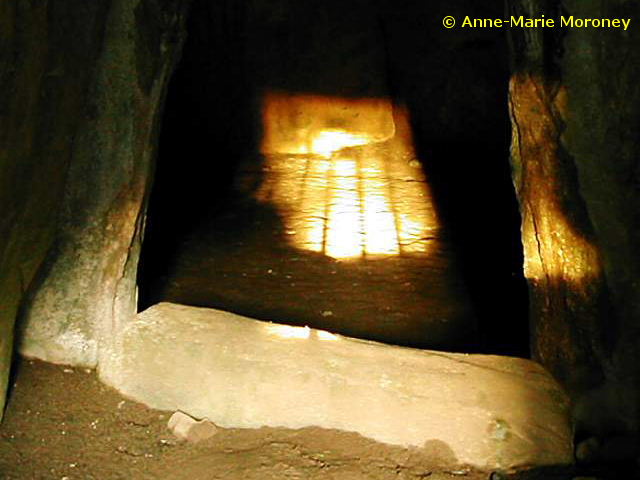 Winter sunbeam on the floor of the Dowth passage between dark orthostats, sill stone in the foreground.