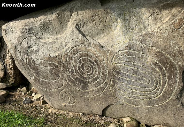Knowth Kerbstone 5 with a central spiral, nested U-shaped grooves and a row of cup marks along the top.