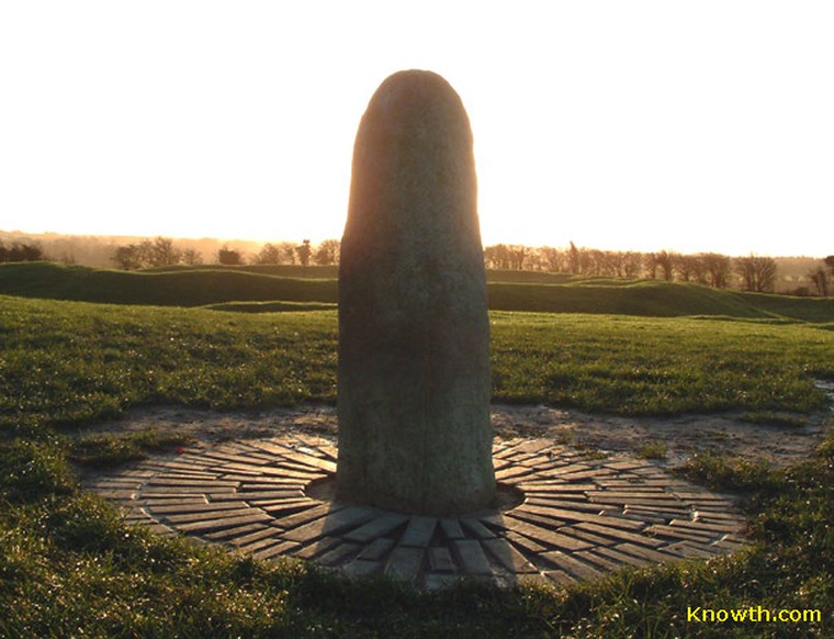 Lia Fáil standing stone on the Hill of Tara silhouetted against a low Samhain sunrise, with circular paving and frosty grass in the foreground.