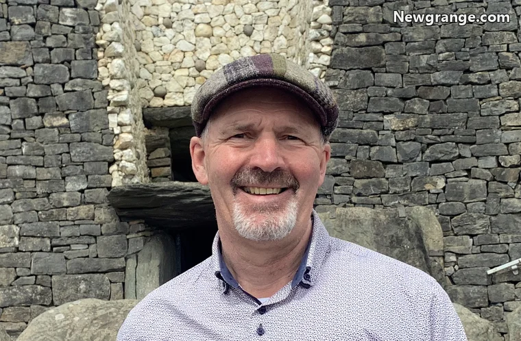 Michael Fox in a flat cap, smiling in front of the quartz facade and entrance at Newgrange.