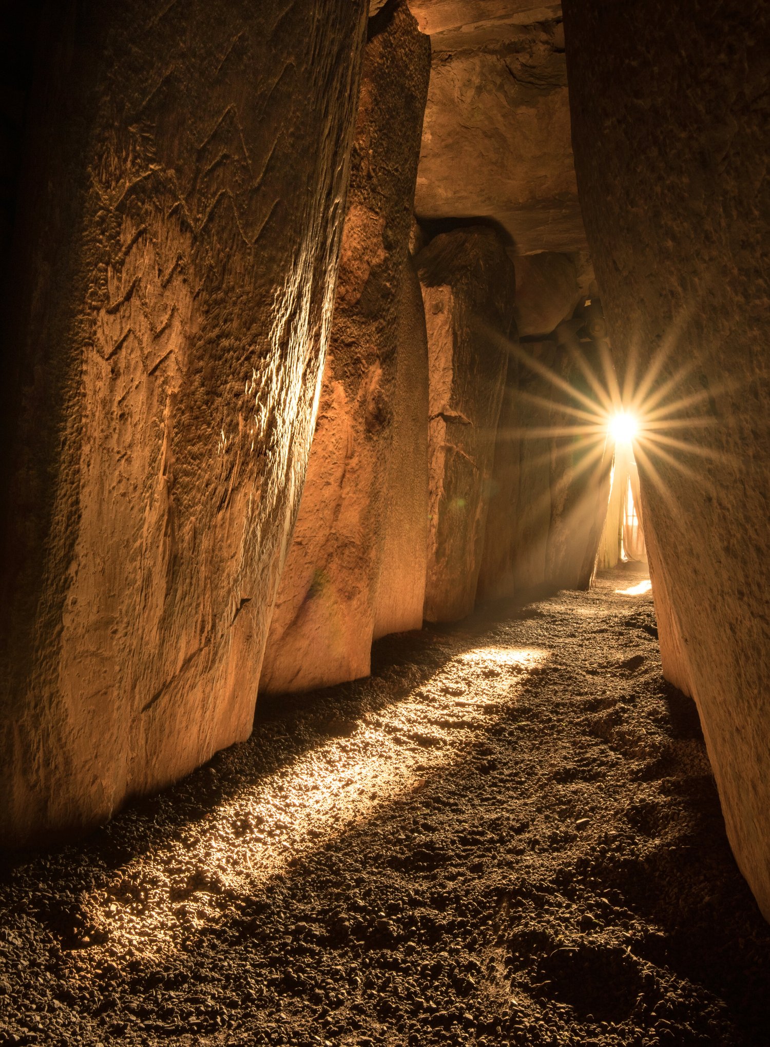 Winter solstice sunlight entering the Newgrange passage, with a starburst at the far end and carved lines lit on the left orthostat.