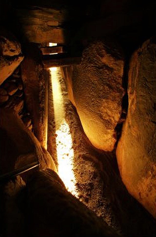 Narrow passage at Newgrange with a golden beam of winter solstice sunlight along the floor between orthostats.