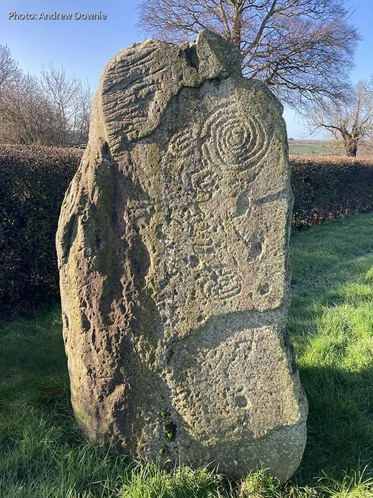 Carved standing-stone from Dowth standing in grass below Newgrange.