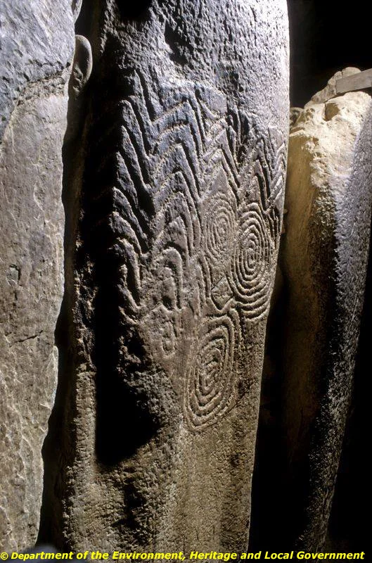 Passage orthostat L19 at Newgrange, with chevrons above three spirals and a heavily pitted surround.